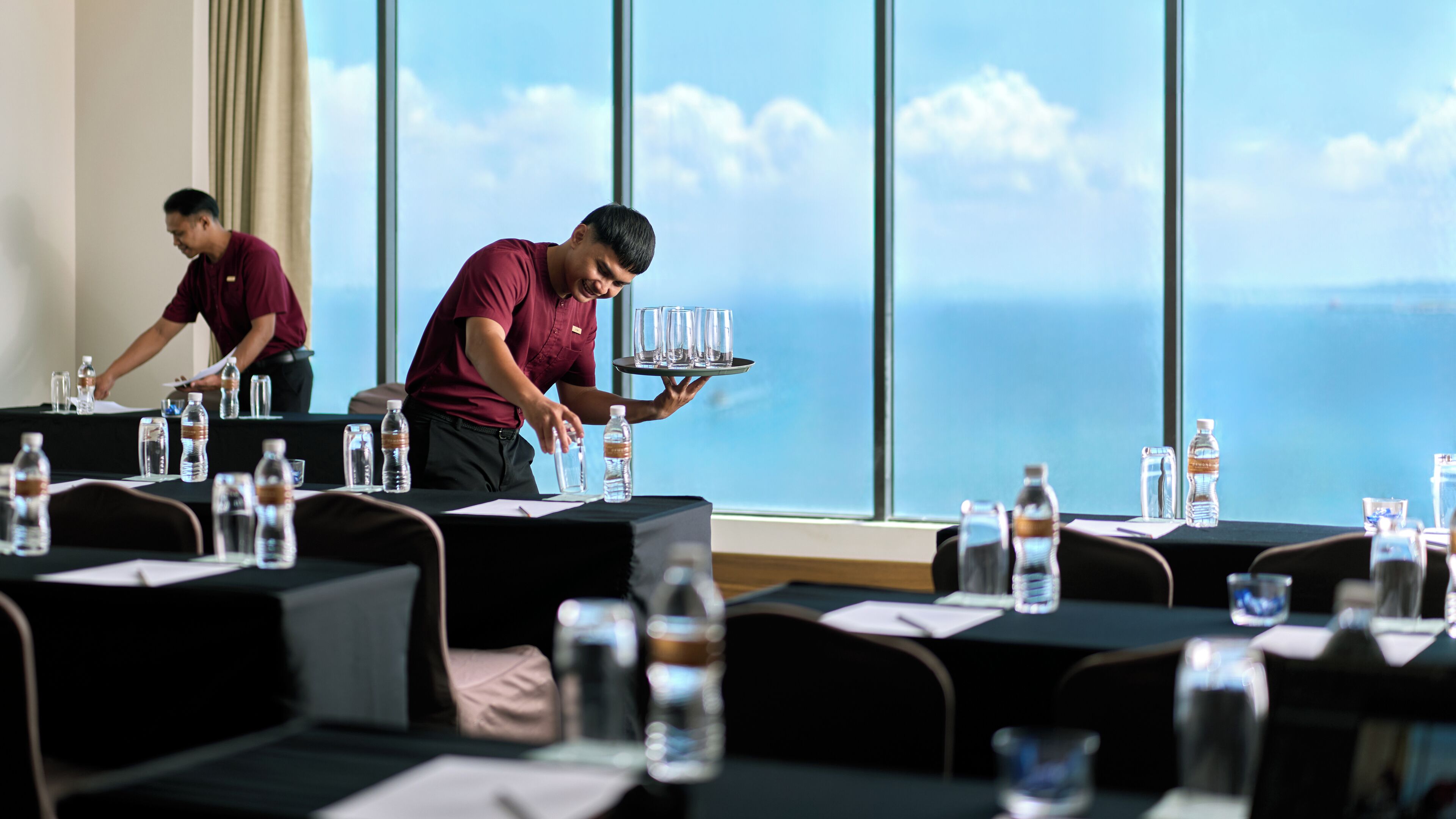 A conference room with tables set for a meeting, water bottles, and a view of the ocean through large windows.