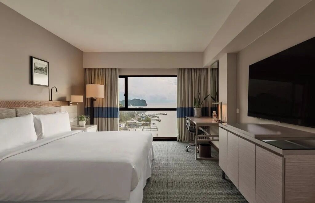 Habitación de hotel con cama, escritorio, televisión y vista a la ciudad.