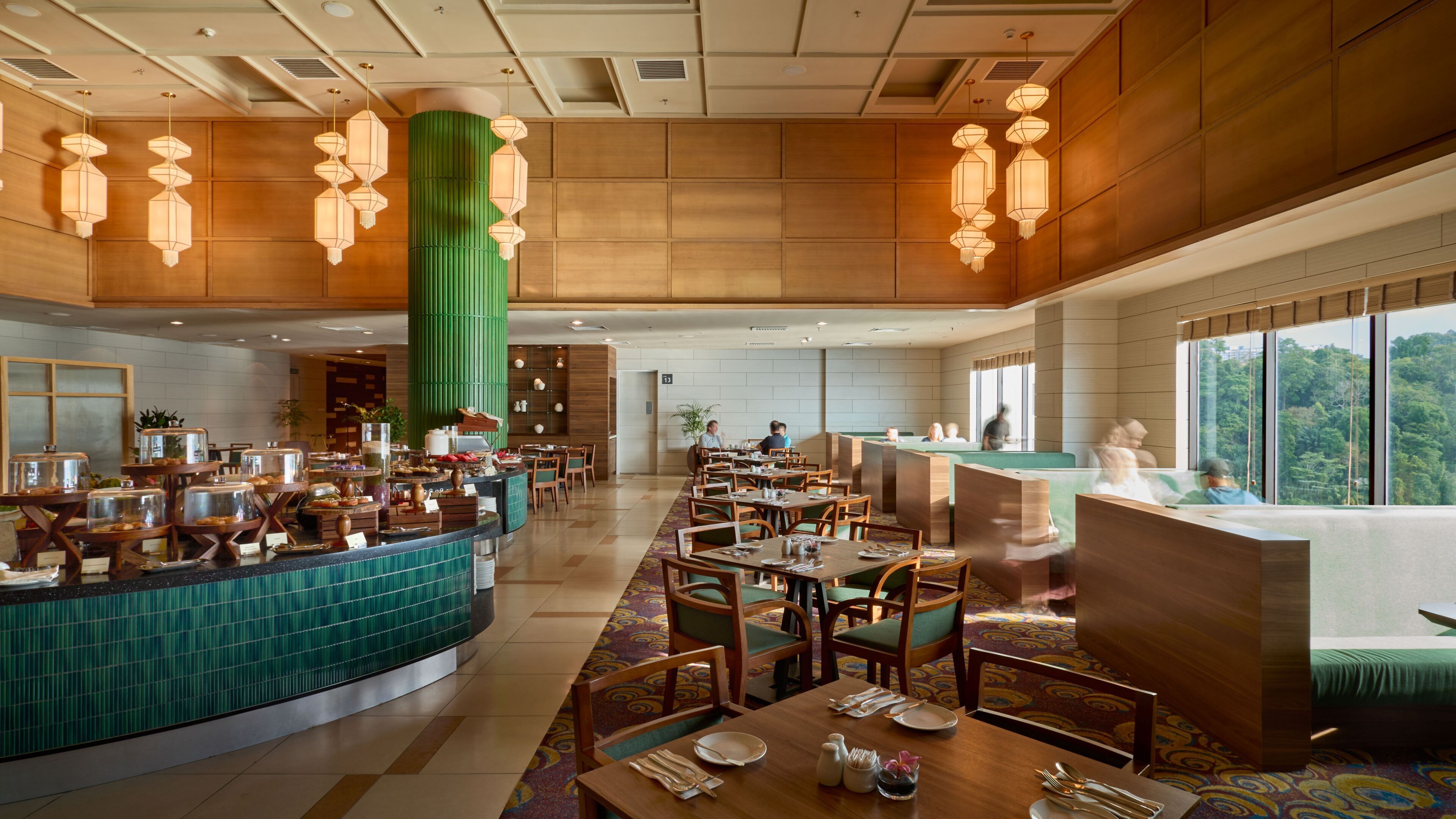 A spacious hotel lobby with a central counter, multiple seating areas, and a large window offering a view of the outdoors.