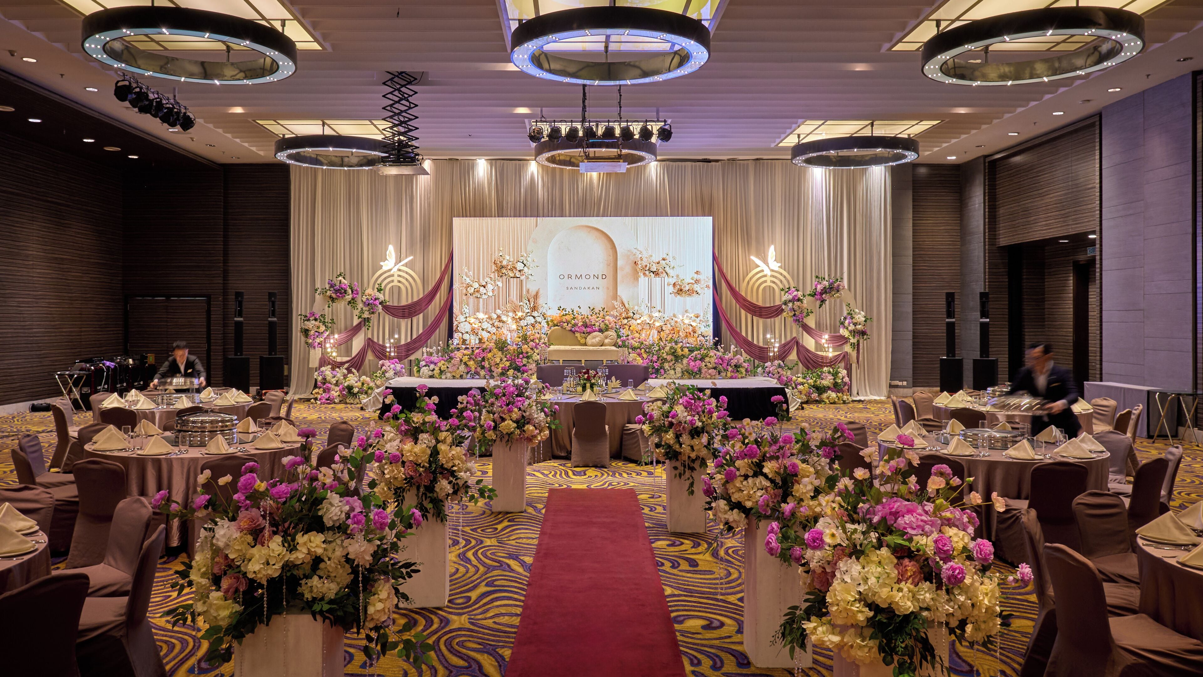 A banquet hall with round tables, a central stage, and floral arrangements.