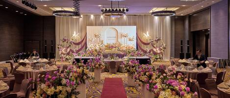 A banquet hall with round tables, a central stage, and floral arrangements.