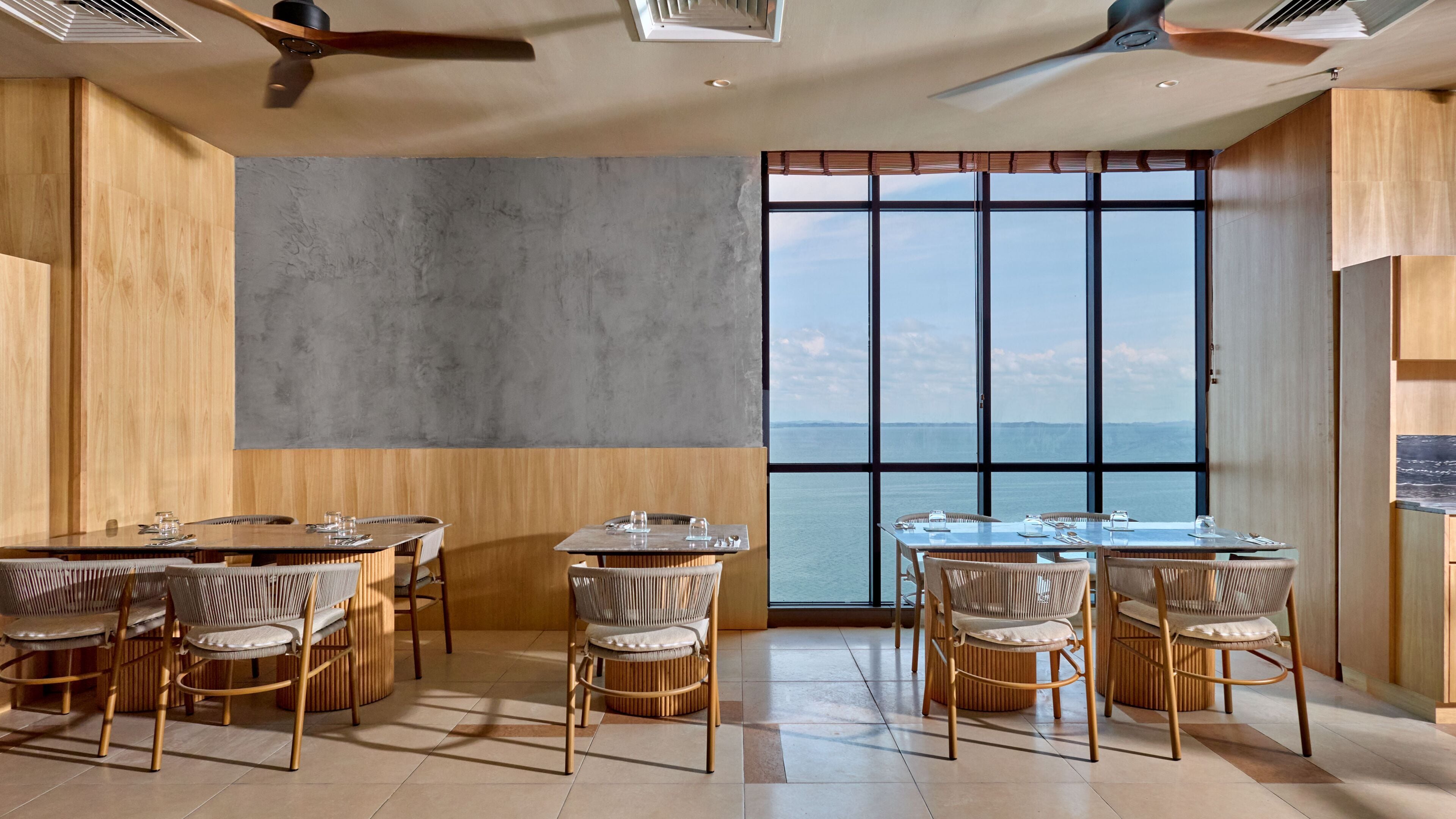 A dining area with a view of the sea, wooden walls, and ceiling fans.