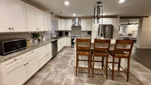 Una cocina moderna con armarios blancos, encimera de granito, refrigerador de acero inoxidable y un comedor con sillas de madera.