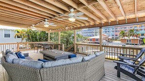 Une terrasse extérieure couverte, aménagée avec des meubles en osier, des ventilateurs de plafond et offrant une vue sur les bâtiments en arrière-plan.