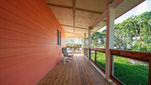 Una terrazza in legno coperta con ringhiera, una sedia e vista su un paesaggio verde.