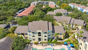 Un hotel con piscina, varios balcones y vistas a la vegetación circundante y al paisaje urbano.
