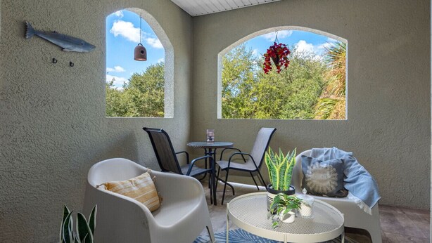 Un patio acogedor con una silla blanca, una mesa redonda y una planta colgante.