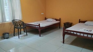 A room with two wooden beds, a chair, a small trash bin, and a window with curtains.