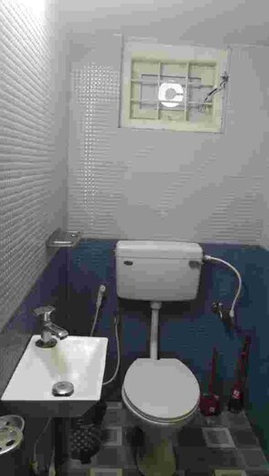 Een kleine badkamer met toilet, wastafel en een raam boven het toilet.