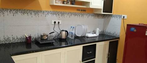 Een koelkast, een kookplaat, een waterkoker, kookgerei, borden en bestek