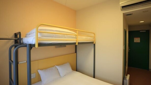 Une chambre avec un lit superposé, un lit simple en bas et un autre en haut. Un climatiseur mural est fixé au mur, sur la droite.