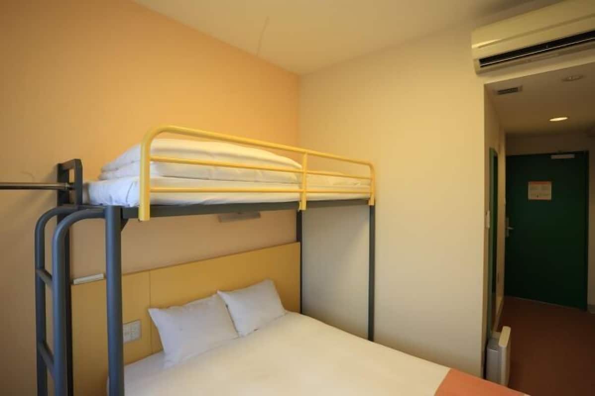 A bunk bed room with a single bed below and a bunk bed above. There is a wall-mounted air conditioning unit to the right.