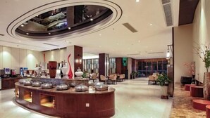 A modern hotel lobby with a central reception desk, seating area, and a large glass window.