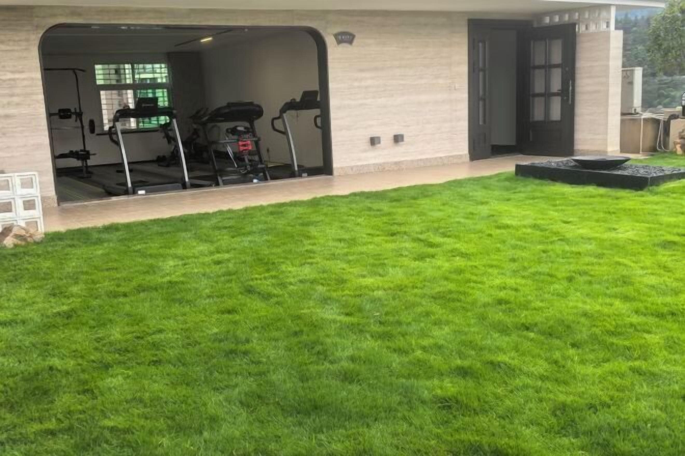 A house with a covered outdoor area, a well-maintained lawn, and a garage with exercise equipment.
