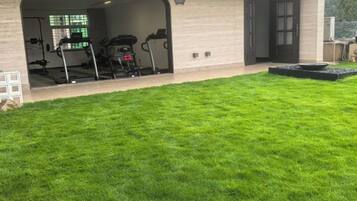 A house with a covered outdoor area, a well-maintained lawn, and a garage with exercise equipment.