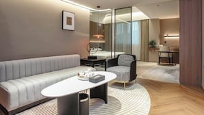 A modern hotel room with a sofa, a round table, a chair, a desk, and a mirror.
