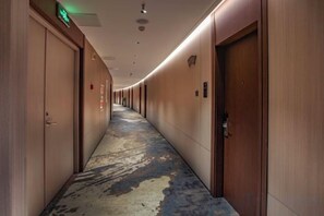 A hotel corridor with doors on both sides, a patterned floor, and a ceiling with recessed lighting. - Jiaxing Hotel (Jian'ou)