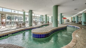 An indoor swimming pool with tiled edges, surrounded by green pillars and a seating area with tables and chairs. - Oceanfront Condo Gorgeous View&Pools (Myrtle Beach)