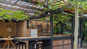 A rustic outdoor bar area with wooden furniture, a bar counter, and a pergola with vines. - 5 Star Holiday Home in Nakskov (Nakskov)