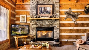 A cozy log cabin interior with a stone fireplace, a television, and a dining area with a table set for two. - Up The Creek Cabin - Peaceful surroundings on a mountain stream (Sevierville)