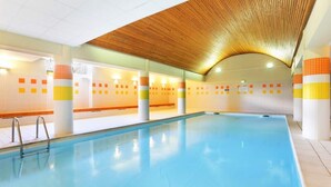 An indoor swimming pool with clear water, wooden ceiling, and tiled walls with orange and yellow accents. - Holiday Home in Ax-les-thermes With Spa (Ax-les-Thermes)