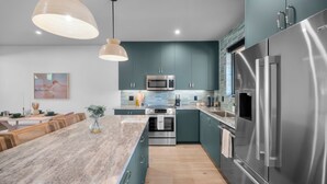 Una cocina moderna con armarios verde mar, electrodomésticos de acero inoxidable, una isla de mármol e iluminación colgante.