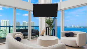 Un soggiorno moderno con un grande televisore, due divani, un tavolino rotondo e vista sulla città e sul mare.