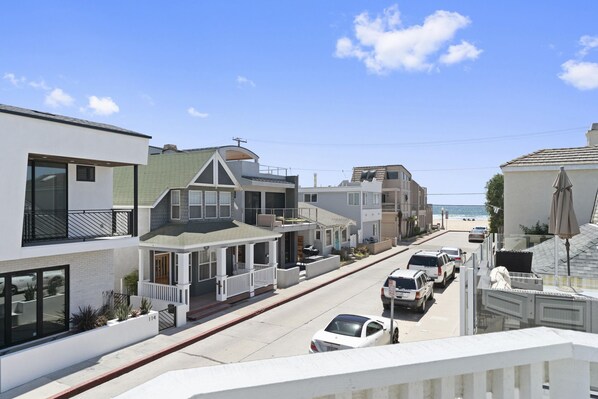 A coastal street with modern houses, a clear sky, and a beach in the distance.