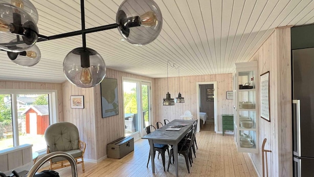 Uma cozinha moderna com ilha central, piso de madeira e área de jantar com mesa comprida e cadeiras.