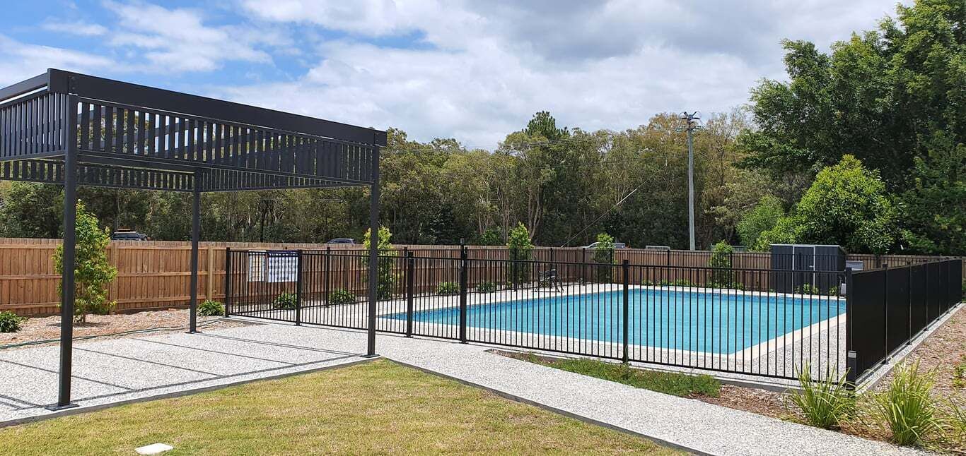Un patio trasero con piscina, cerca de madera y estructura de pérgola.