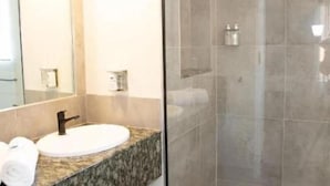 Un baño moderno con encimera de granito, lavamanos blanco y cabina de ducha de vidrio.