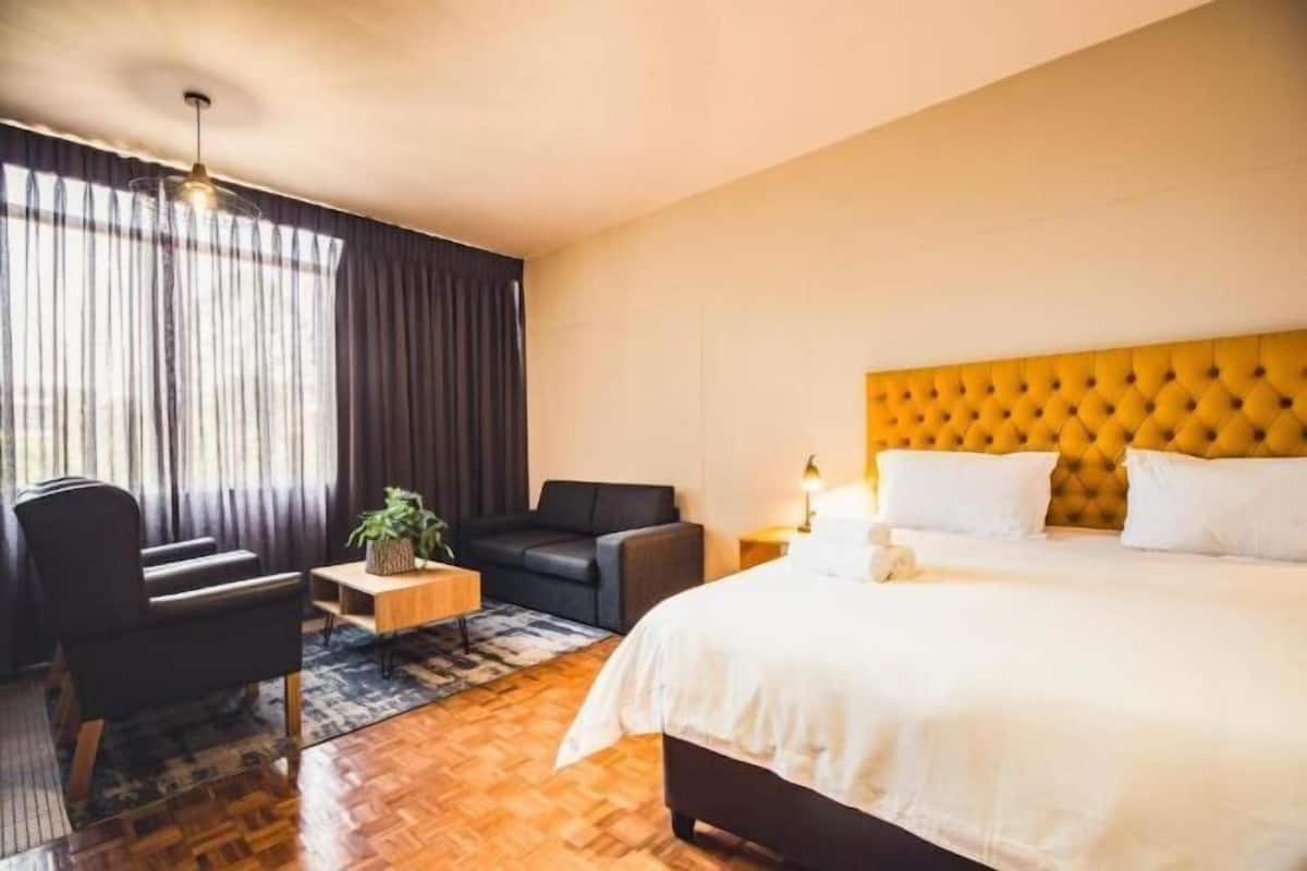 Habitación de hotel con cama, sofá, una mesita y planta en maceta.