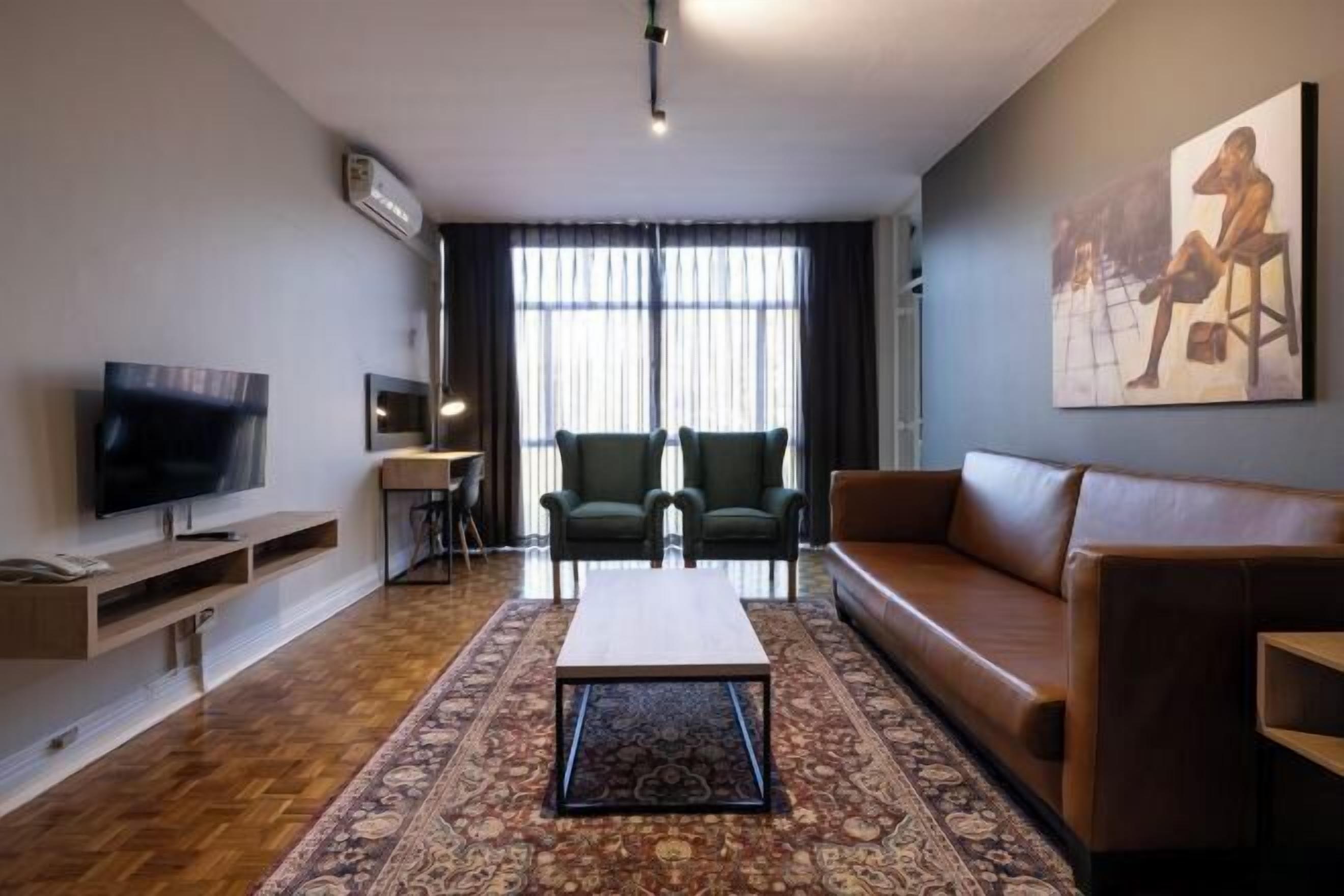 A modern living room with a flat-screen TV, a sofa, a coffee table, and a patterned rug.