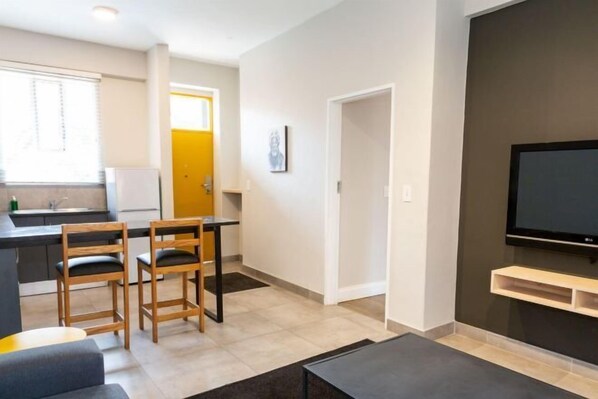 A modern living room with a flat-screen TV, a sofa, and a dining area with chairs and a table.