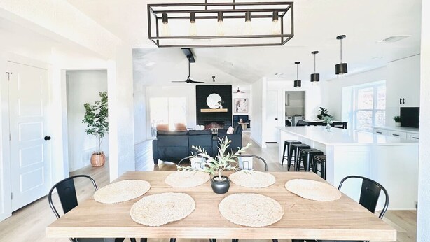 A modern kitchen with a central island, a dining area with a wooden table and chairs, and pendant lighting.