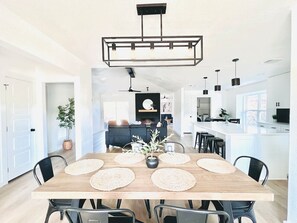 Una cocina moderna con una isla central, una zona de comedor con mesa y sillas de madera, e iluminación colgante.