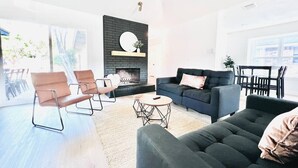 A modern living room with a fireplace, a sofa, a coffee table, and a dining area.