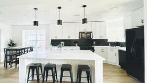 A modern kitchen with a large island, black bar stools, white cabinets, and black appliances.