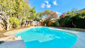 A swimming pool with a curved edge, surrounded by a wooden fence and trees.