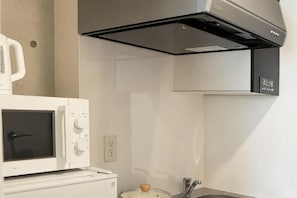 A kitchen with a microwave, a stove, and a built-in oven. - Poka Stay Kamata (Tokyo)
