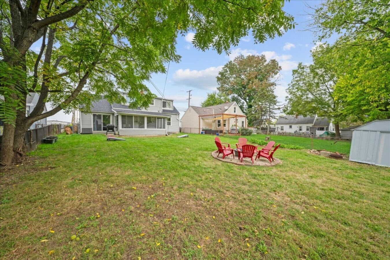 A backyard with a lawn, a patio with chairs, and a house in the background.
