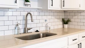 A kitchen with white cabinets, a stainless steel sink, and a beige countertop. - Group Ready 4BR near OSU w/ Fire Pit & Wet Bar (Columbus)