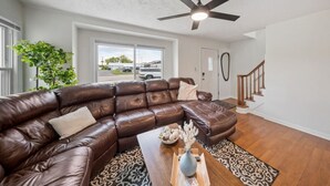 A living room with a leather sectional sofa, a ceiling fan, a wooden coffee table, and a view of the outside. - Group Ready 4BR near OSU w/ Fire Pit & Wet Bar (Columbus)