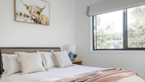 Une chambre avec un grand lit, une fenêtre donnant sur des arbres et un tableau représentant un taureau accroché au mur.