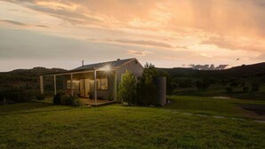 Une maison moderne dotée d’un porche abrité, entourée d’un champ verdoyant et avec des collines en arrière-plan.