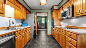 Una cocina con armarios de madera, un refrigerador de acero inoxidable, un microondas y un lavamanos.
