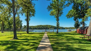 Un parque con un sendero de concreto que lleva a un lago, rodeado de árboles y un área de picnic.