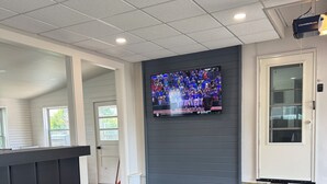 Un área de recepción con televisor, sillas negras y suelo de concreto.