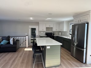 A modern kitchen with a central island, stainless steel appliances, and a dark-colored sofa with patterned cushions.