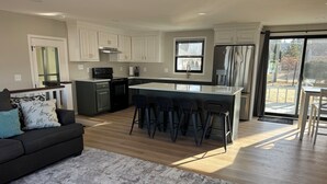 Una cocina moderna con armarios blancos, una isla central con taburetes y un ventanal corredero a un balcón.